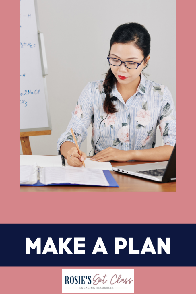 Teacher writing with her computer and plan book that are open